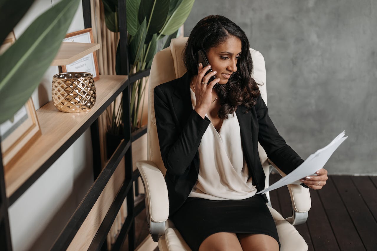 Auf dem Bild ist eine Frau zu sehen, sie sitzt und telefoniert während sie auf ein Dokument guckt. Dieses Bild soll eine typische Szene aus einem Closer Job darstellen.