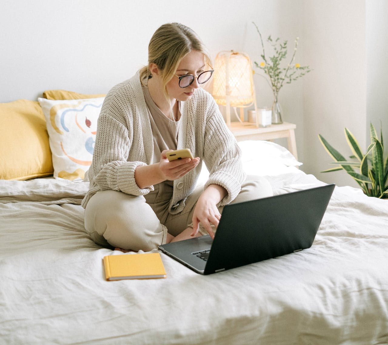 Eine Frau sitzt mit dem Laptop auf dem Bett. Eine Klischee Szene von einem Freelancer 